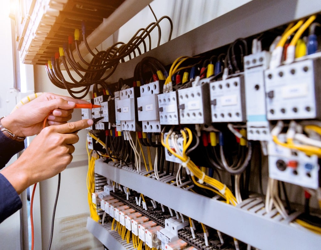 Electrician measurements with multimeter testing current electric in control panel.